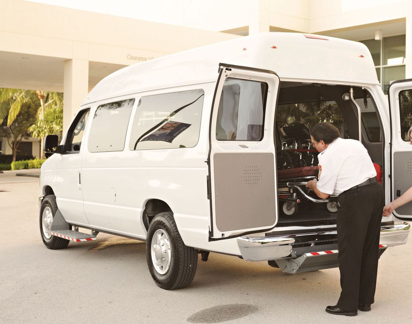 Two emergency responders load a stretcher into an ambulance outside a medical facility.