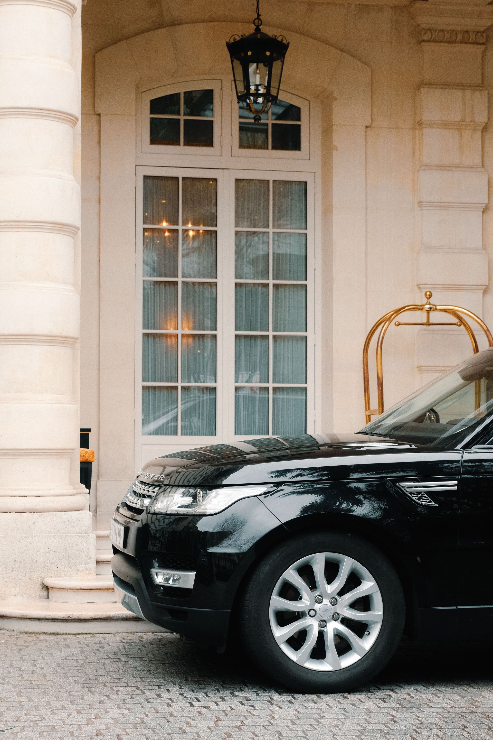 Close-up of a black luxury car parked in front of an elegant building entrance with large windows and pillars.